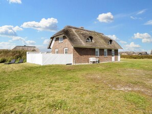 Una casa de techo de paja con fachada de ladrillo, cerca blanca y césped.