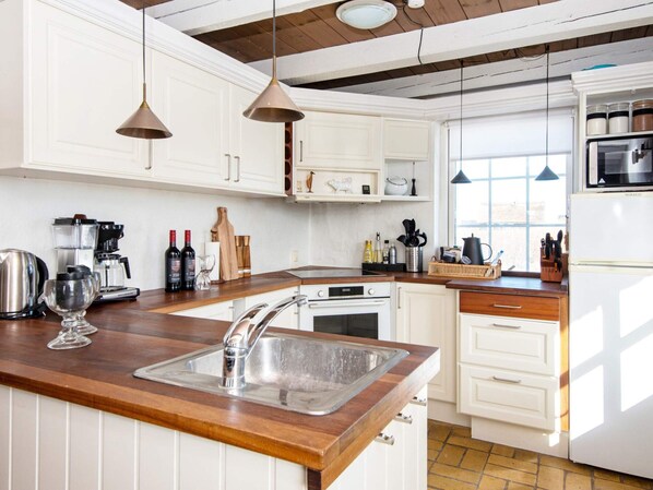 A kitchen with white cabinetry, a wooden countertop, a stainless steel sink, a stove, and a refrigerator.