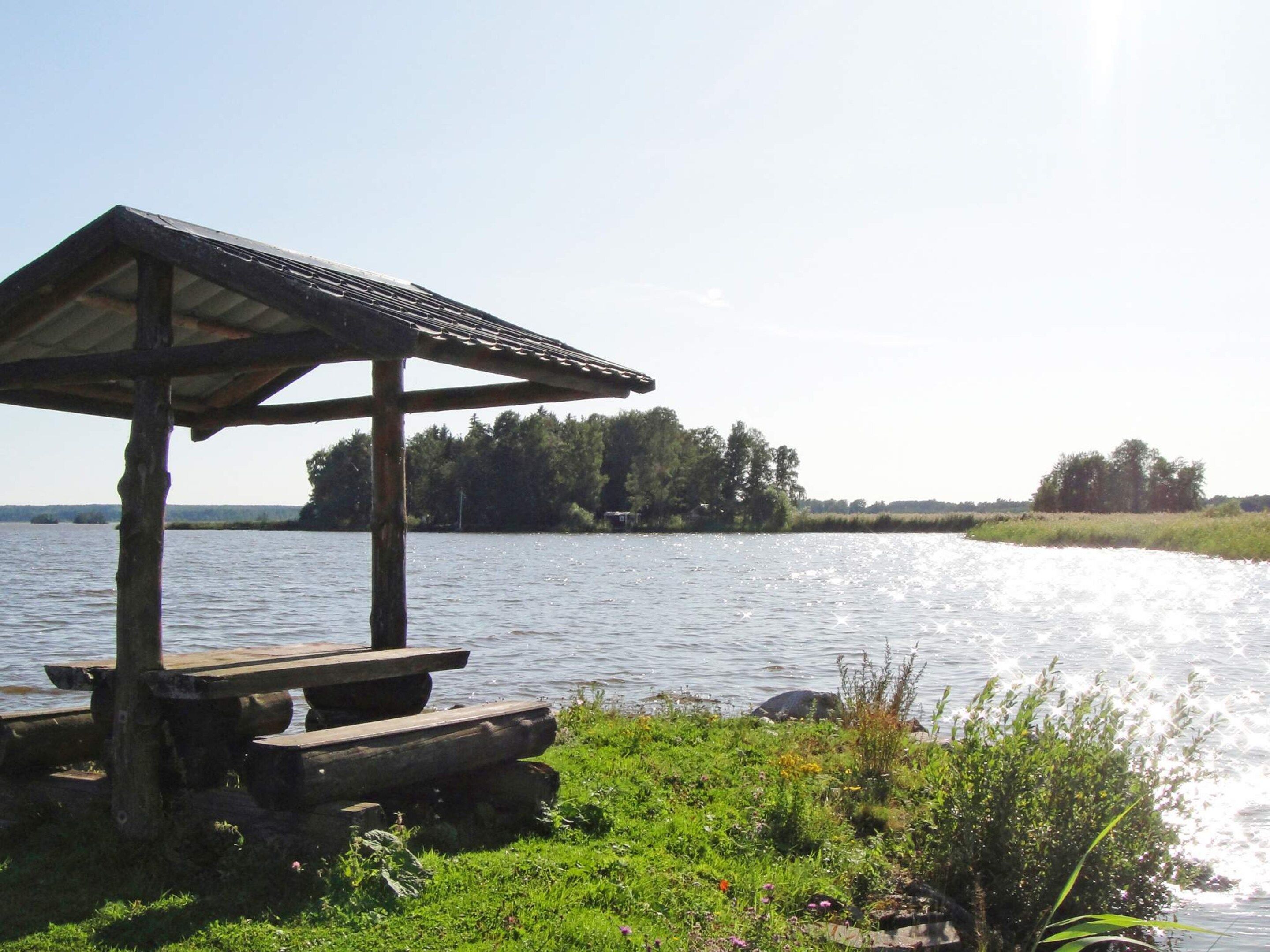En träkonstruktion med tak, eventuellt en lusthus, nära ett vattendrag där en båt syns.
