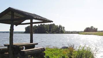 En träkonstruktion med tak, eventuellt en lusthus, nära ett vattendrag där en båt syns.