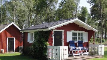 A red cabin with a porch, two chairs, and a small deck.