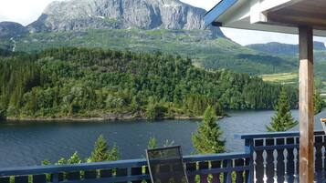 Relax on the deck overlooking a serene lake and lush forest, with a mountain range in the distance.