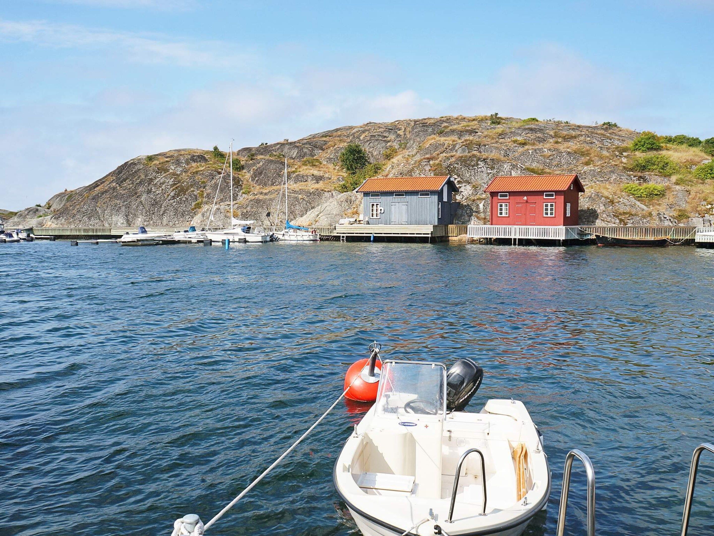 A calm harbor with boats docked, a small boat tied to a dock, and a red building with a white fence.