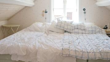 A bedroom with a sloped ceiling, a bed with white bedding, a small bedside table, and a window with a view of the outside.