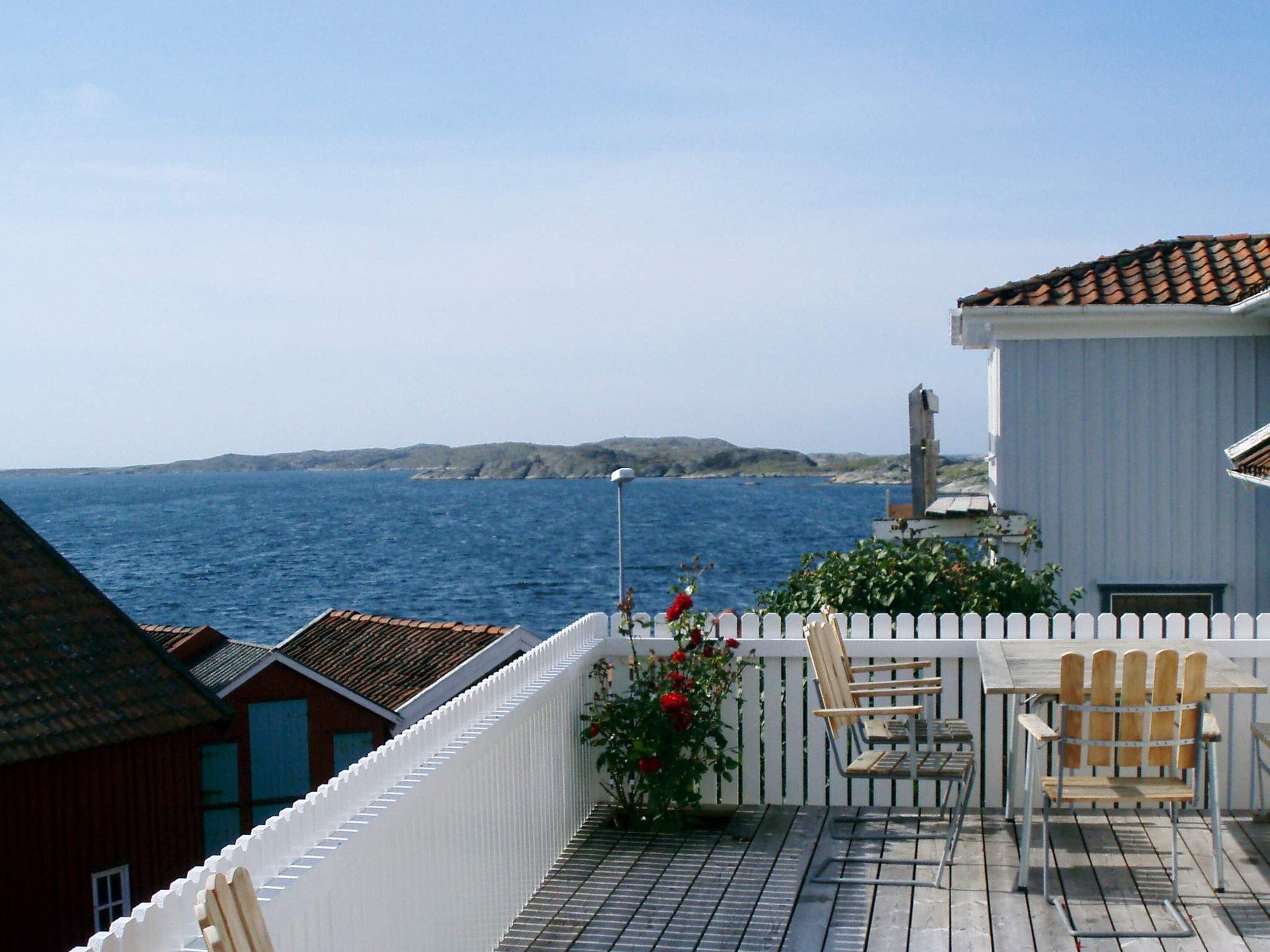A balcony with a view of the sea, a white fence, and a table with chairs.