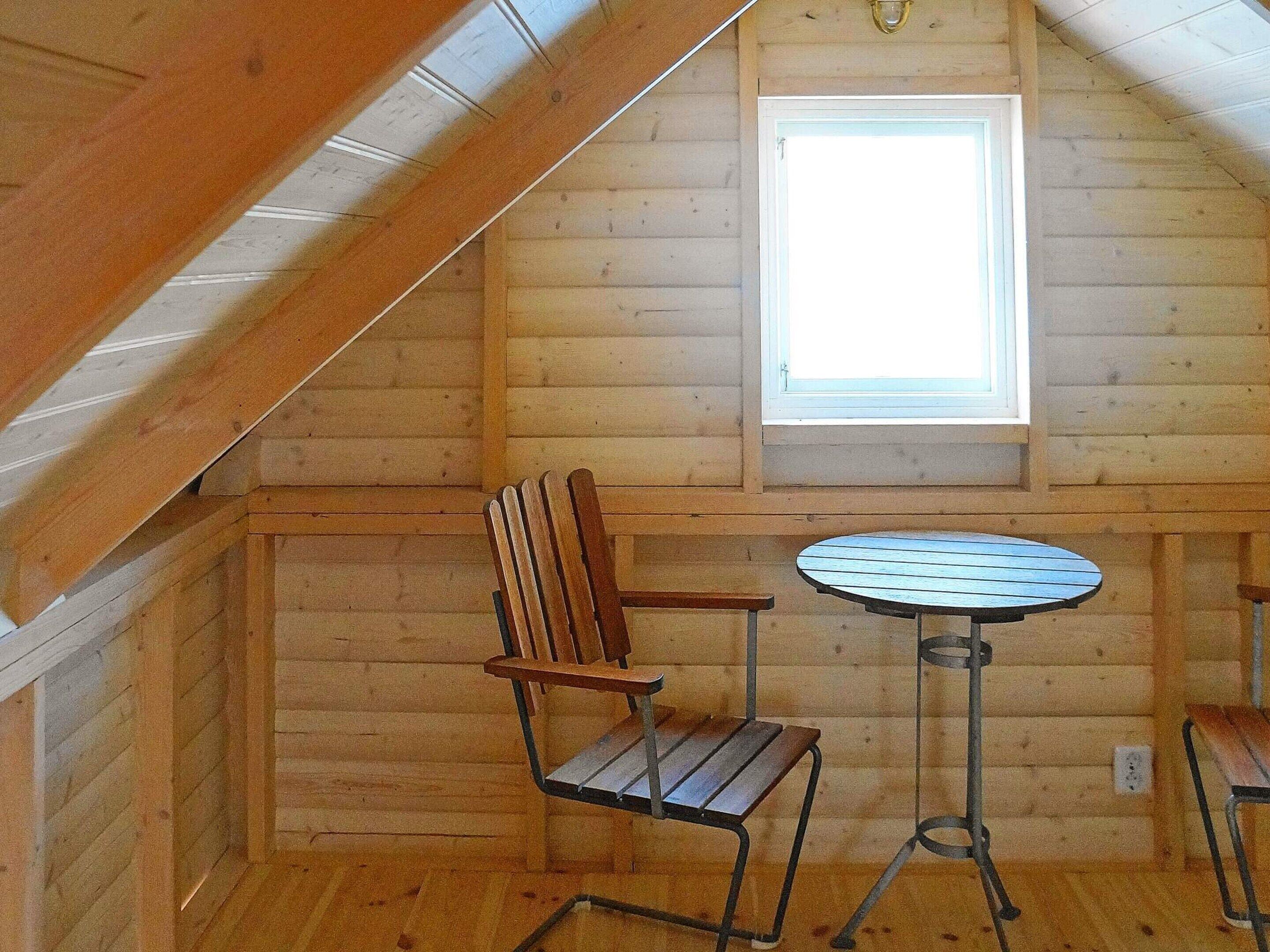 A wooden cabin interior with a sloped ceiling, a window, a round table, and two chairs.