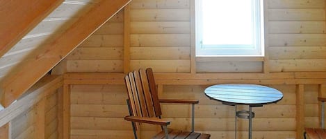 A wooden cabin interior with a sloped ceiling, a window, a round table, and two chairs.