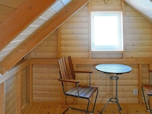 A wooden cabin interior with a sloped ceiling, a window, a round table, and two chairs.