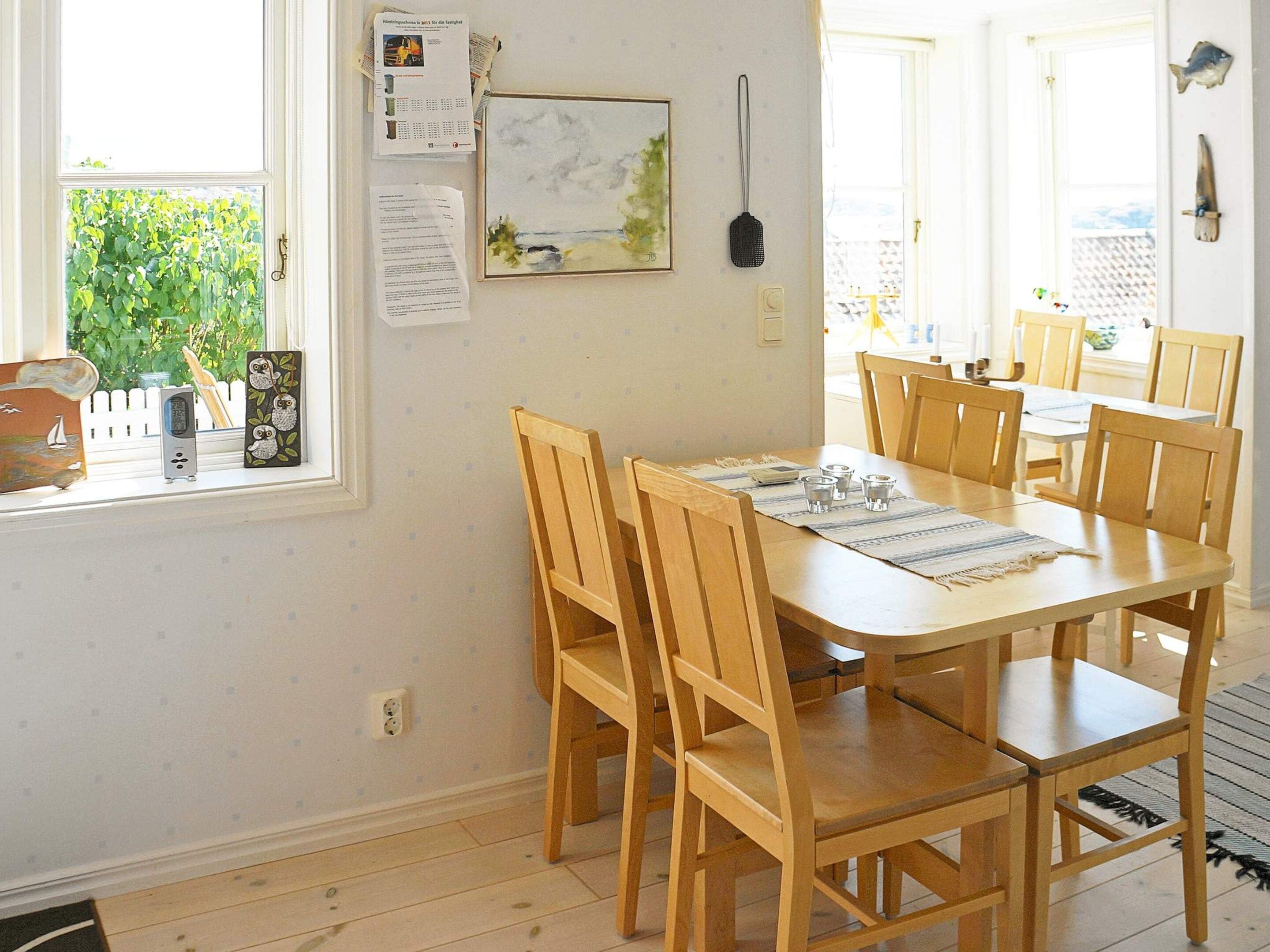 A dining area with a wooden table and chairs, a window with a view of greenery, and a wall-mounted painting.