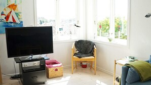 A living room with a flat-screen TV, a wooden chair, a blue sofa, and a window with a view of buildings. - Holiday Home in HÃ¤lleviksstrand (Hälleviksstrand)