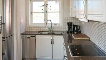 A modern kitchen with stainless steel appliances, a window with blinds, and a coffee maker on the counter.