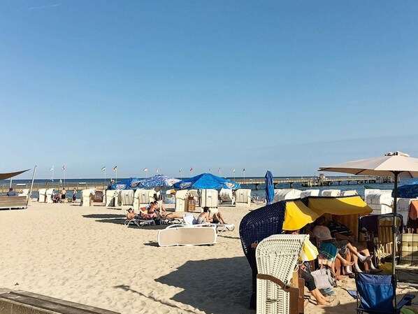 A beach with rows of beach chairs and umbrellas, a pier in the background, and a clear sky.
