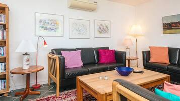 A living room with a black sofa, a wooden coffee table, a red lamp, a bookshelf, and a patterned rug.