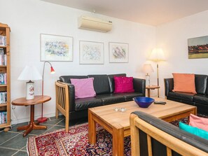 A living room with a black sofa, a wooden coffee table, a red lamp, a bookshelf, and a patterned rug. - 4 Star Holiday Home in Haderslev (Haderslev)