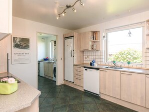 A modern kitchen with a dishwasher, a sink, and a window with plants.