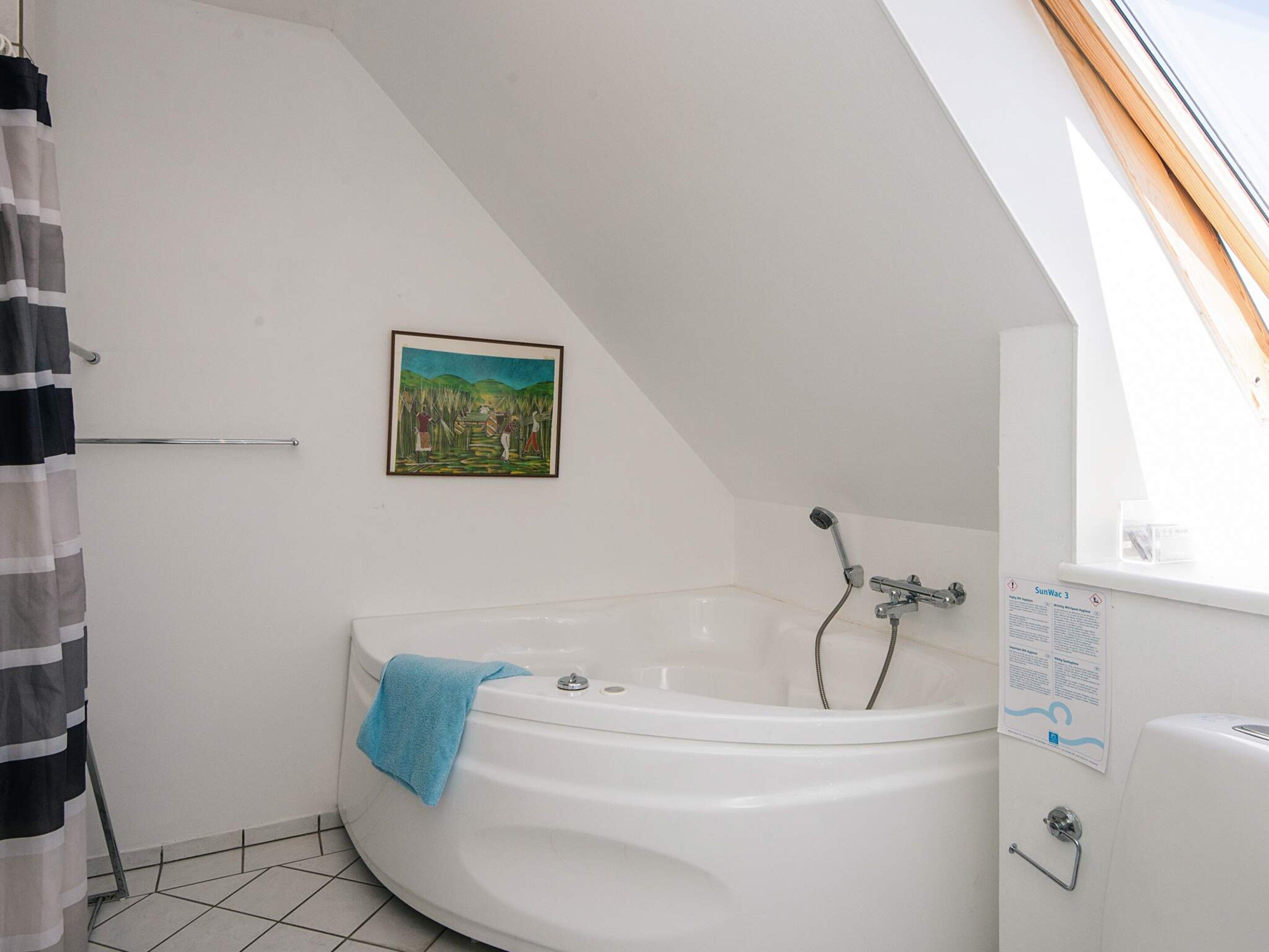 A bathroom with a bathtub, a shower, a towel, a picture on the wall, and a window.