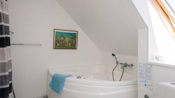 A bathroom with a bathtub, a shower, a towel, a picture on the wall, and a window.
