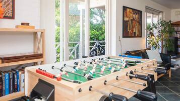 A room with a foosball table, a bookshelf, a sofa, and a painting on the wall.