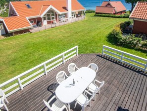 A deck with a table and chairs, overlooking a well-maintained lawn and a house with a red roof. - 4 Star Holiday Home in Haderslev (Haderslev)