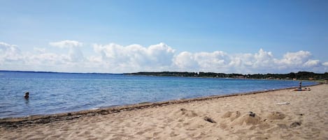A beach with clear blue water, sandy shore, and distant hills.