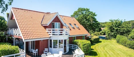 A house with a red-tiled roof, a covered patio with white furniture, and a well-maintained lawn.