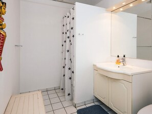 A bathroom with a shower curtain, a sink with soap dispensers, and a mirror.