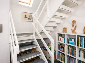 A staircase with white railings, a bookshelf with various books, and a framed picture on the wall.
