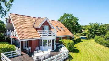 A two-story house with a red-tiled roof, a covered patio with white furniture, and a well-maintained lawn.