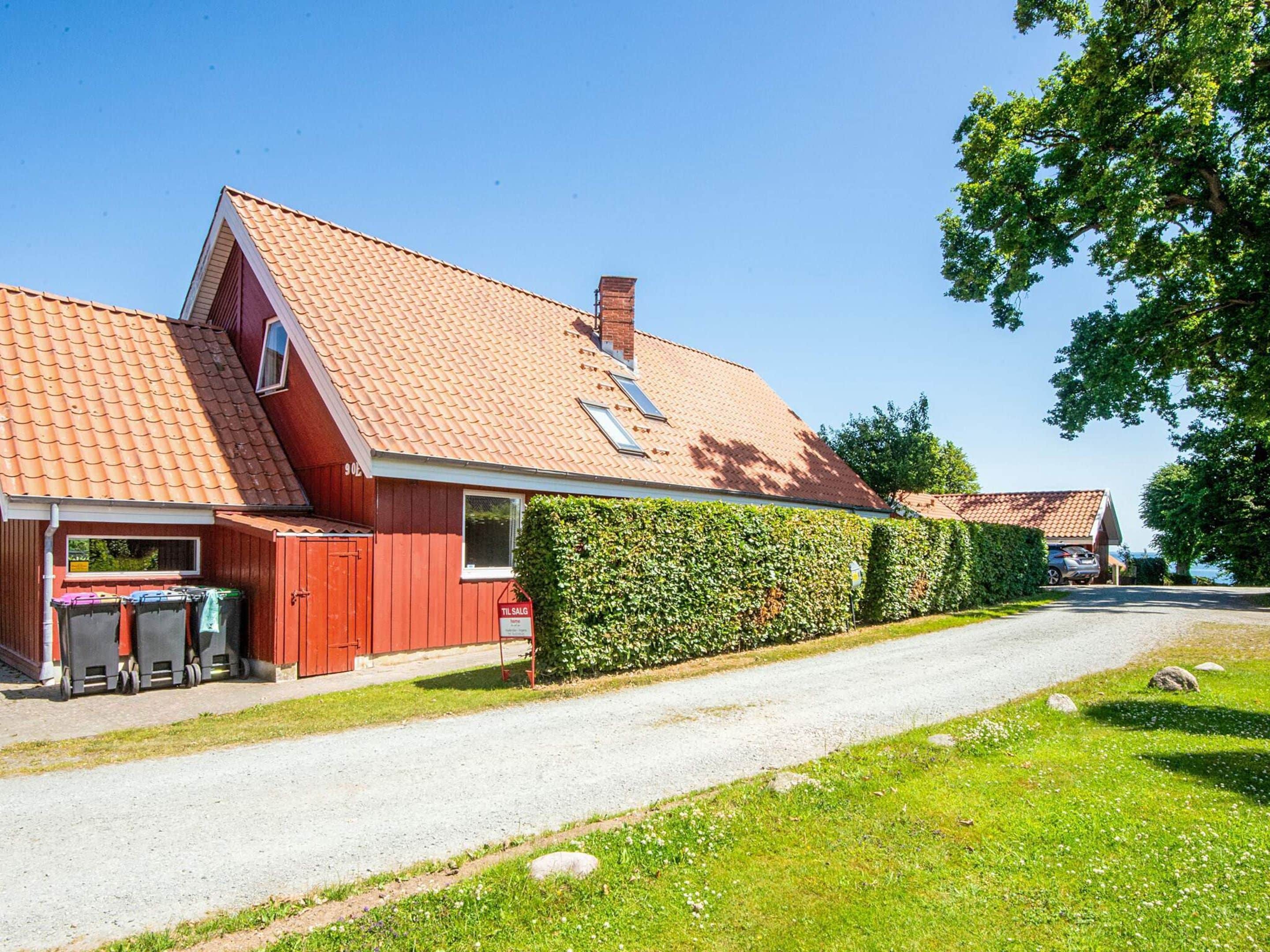 Un bâtiment rouge avec un toit en tuiles, une allée pavée et une haie le long du côté.
