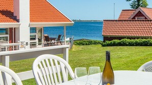 A table with a bottle of wine and glasses, a white chair, and a view of the sea. - 4 Star Holiday Home in Haderslev (Haderslev)