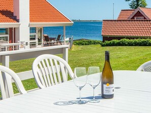 A table with a bottle of wine and glasses, a white chair, and a view of the sea. - 4 Star Holiday Home in Haderslev (Haderslev)