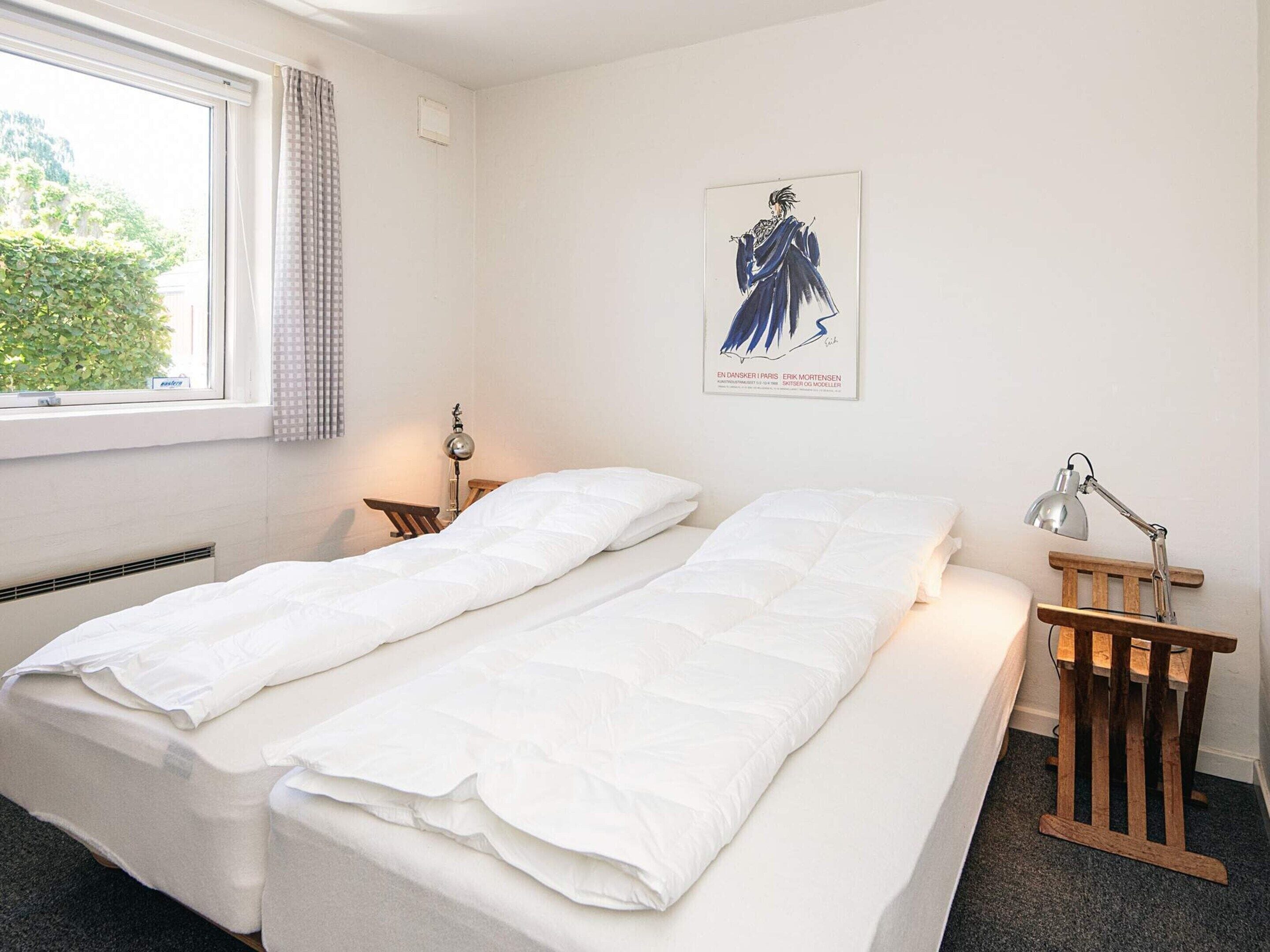 A room with a bed, a desk, a chair, a lamp, and a poster on the wall.
