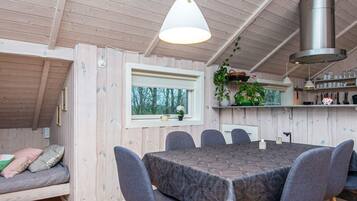 Ein gemütliches Blockhauss-Interieur mit Esstisch, Stühlen, einer Couch, einem Fenster und einer Küchenzeile.