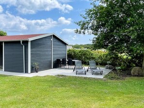 A covered outdoor seating area with a table and chairs, a large tree, and a building with a red roof. - 6 Person Holiday Home in Sydals (Sydals)