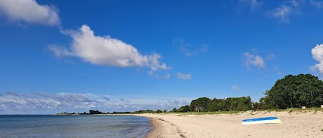 A beach with a clear sky, a sandy shore, and a blue and white boat on the sand.