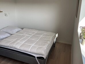 A neatly made bed with a grey mattress and white bedding in a room with wooden flooring and a white wall. - 6 Person Holiday Home in Sydals (Sydals)