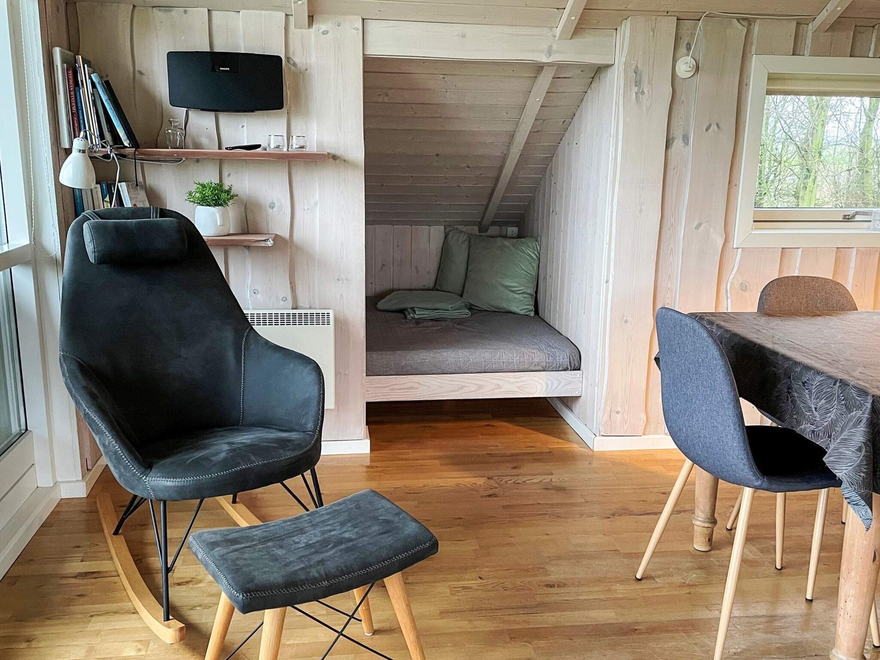 Ein gemütliches Blockhaus-Interieur mit einem schwarzen Ledersessel, einem kleinen Tisch und einem Bett mit grünen Kissen.
