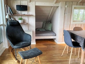 Ein gemütliches Blockhaus-Interieur mit einem schwarzen Ledersessel, einem kleinen Tisch und einem Bett mit grünen Kissen.