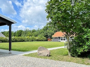 A residential property with a covered outdoor area, a lawn, and a house with a red roof.