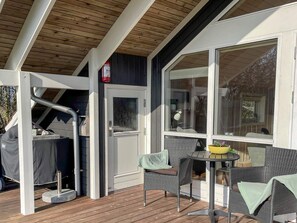 Een overdekt buitengebied met een tafel, stoelen, een overdekte barbecue en een brandblusser.