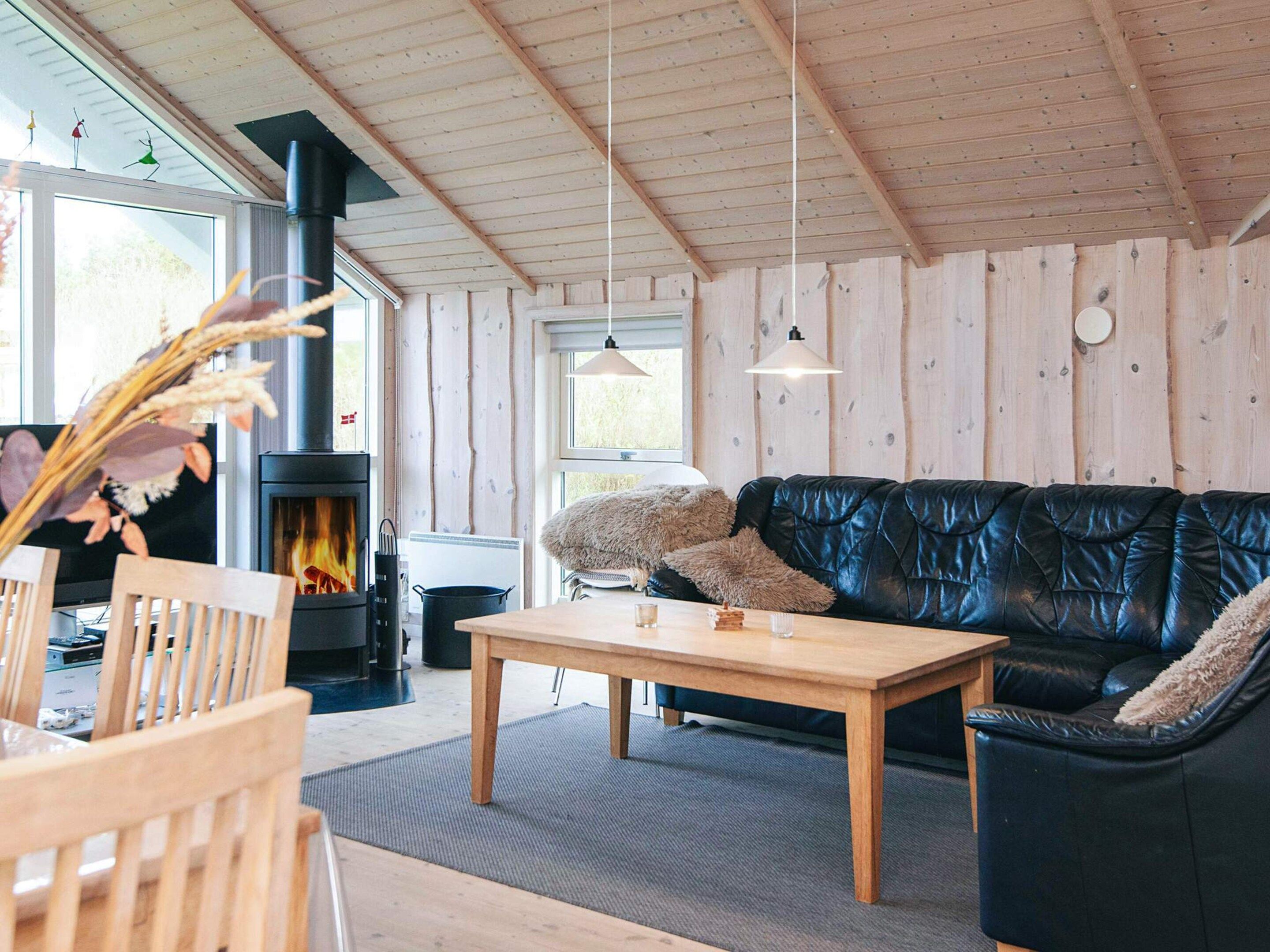 A cozy living room with a fireplace, wooden furniture, and a black leather sofa.