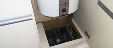 A water heater in a utility room with exposed pipes and a vent.