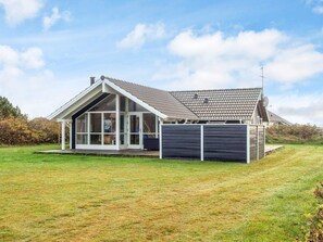 Une maison moderne dotée d’un grand porche vitré, d’un toit en pente et d’une cour clôturée.