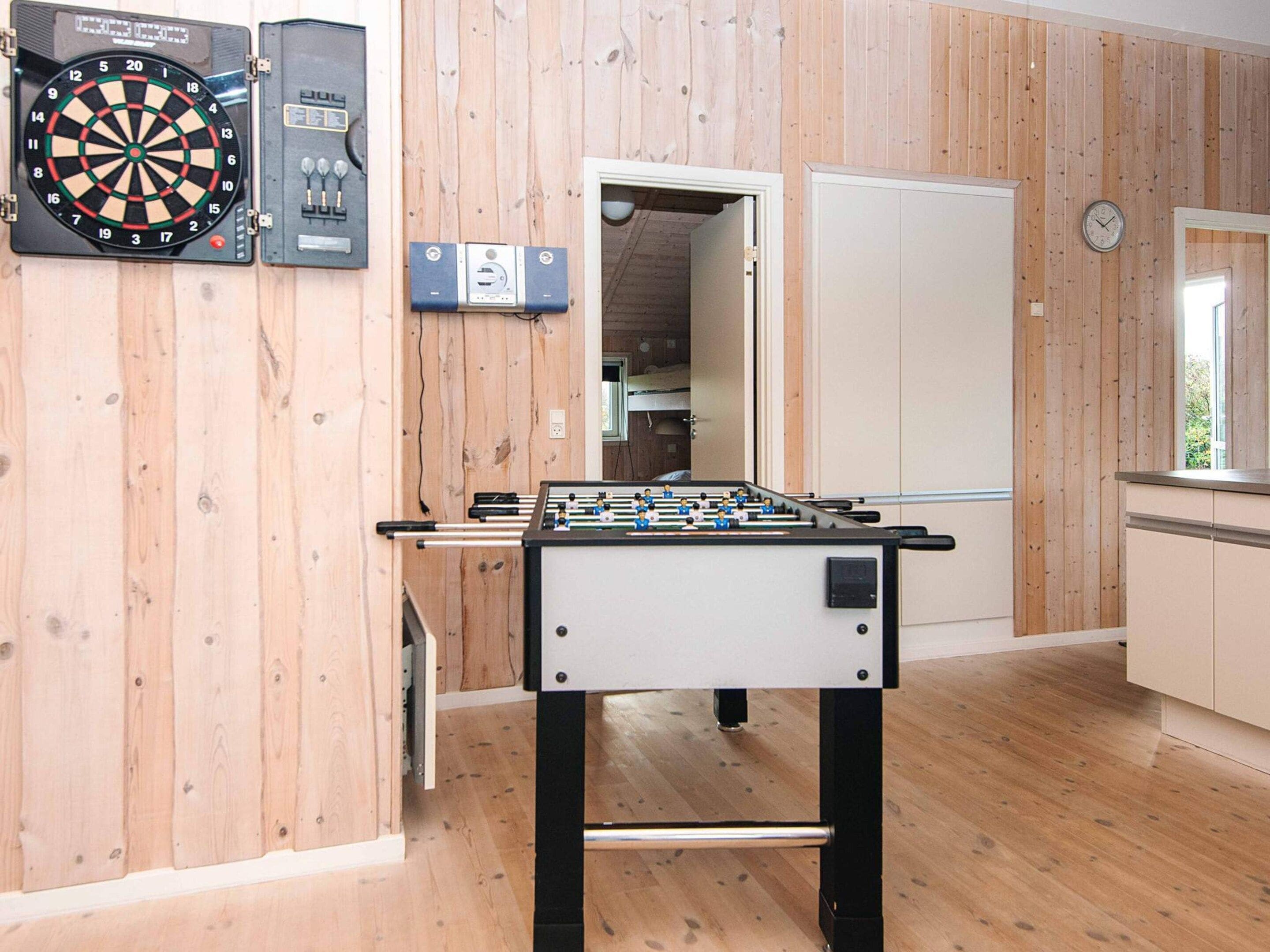 A room with a foosball table, a dartboard, and a clock on the wall.