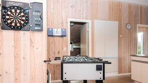A room with a foosball table, a dartboard, and a clock on the wall.
