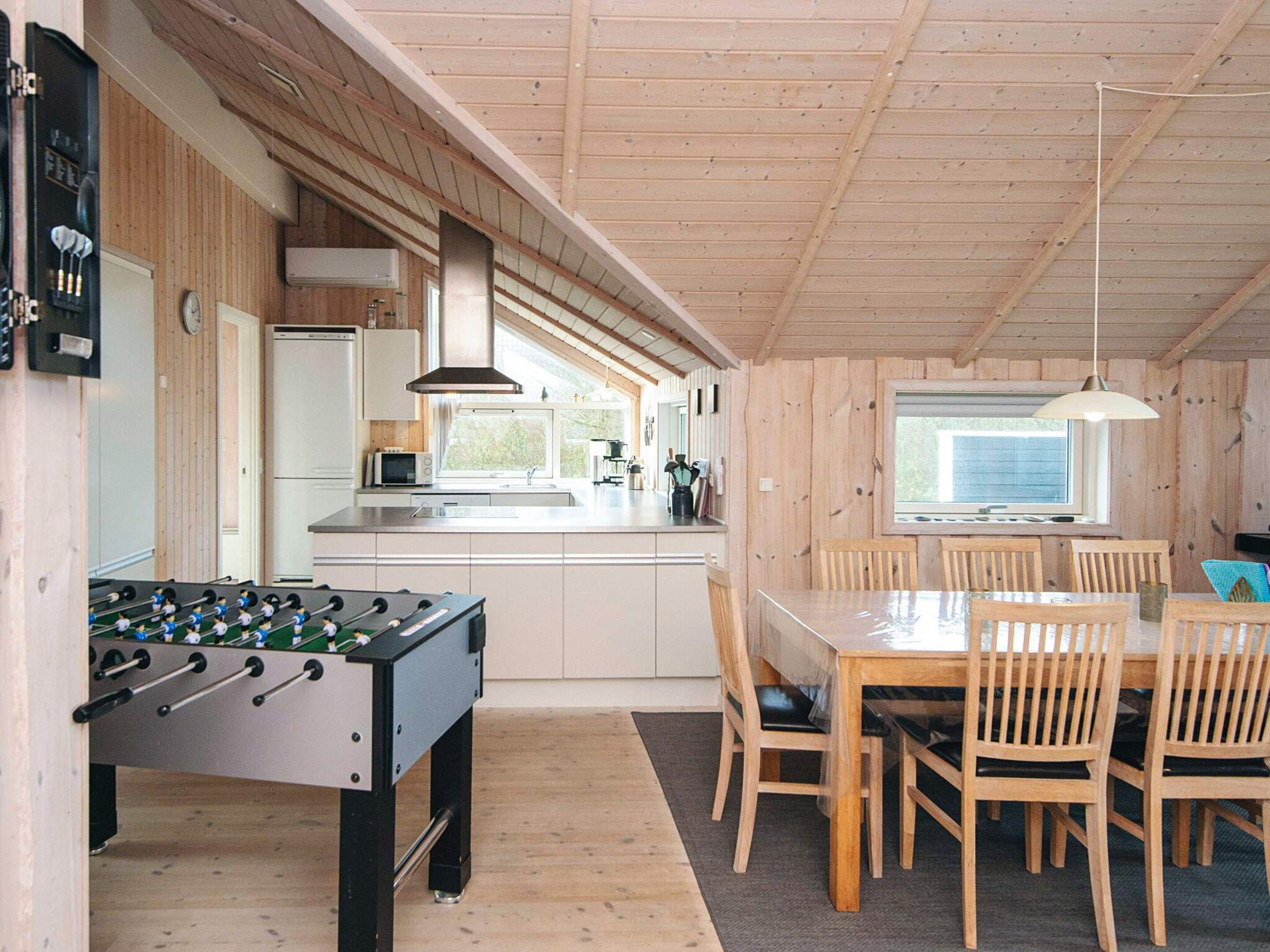 Une cuisine chaleureuse aux murs en bois, avec un baby-foot et un coin repas comprenant des chaises et une table.