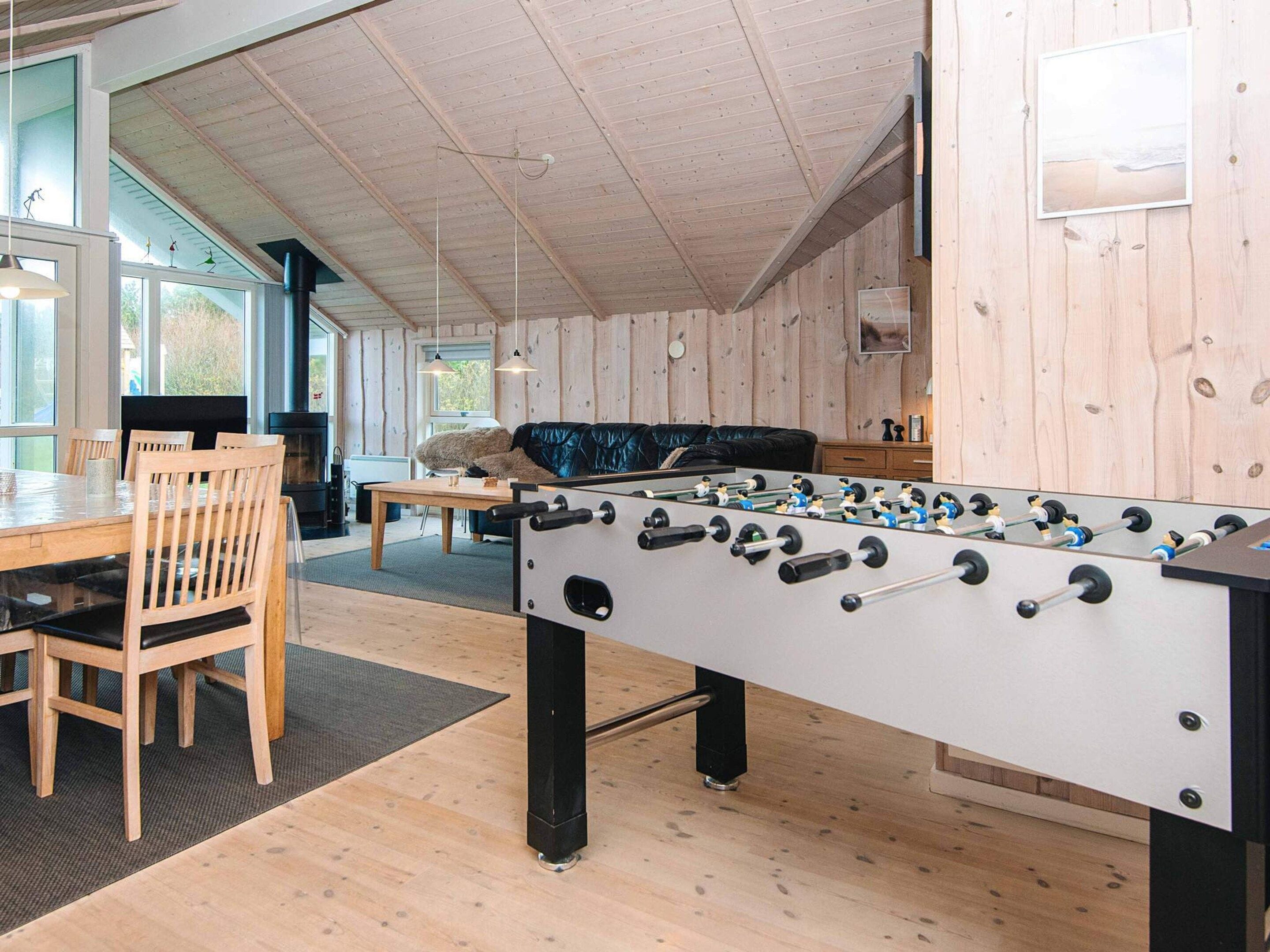A room with a foosball table, wooden furniture, and a large window.