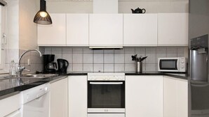A modern kitchen with white cabinets, a stainless steel refrigerator, a microwave, a stove, and a coffee maker. - Luxurious Cabin With Pool in Ringkøbing (Ringkobing)