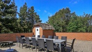 An outdoor patio with a brick wall, a thatched-roof structure, and a table with chairs. - Luxurious Cabin With Pool in Ringkøbing (Ringkobing)