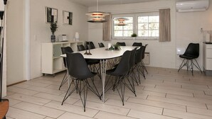 A dining area with a white table and black chairs, a pendant light, and a window with curtains. - Luxurious Cabin With Pool in Ringkøbing (Ringkobing)